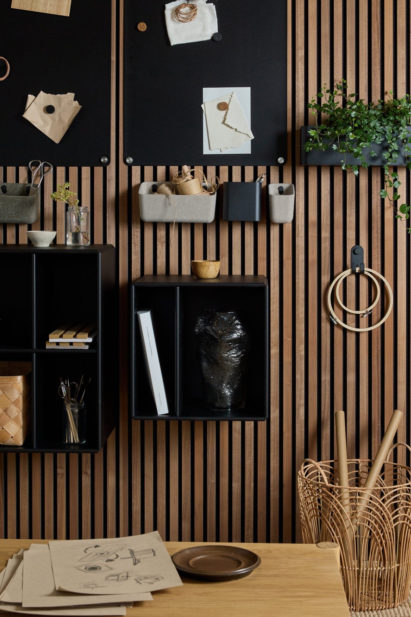 Modern workspace with WoodUpp’s black Arka Bookcase, Danish furniture, acoustic wood slat walls, art supplies, plants, sketches, and organized storage.